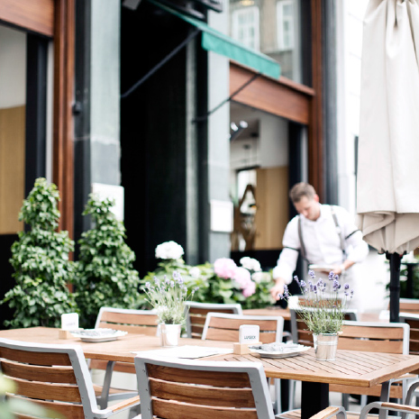 Außenbereich des Restaurants Lugeck: gedeckte Tische, Pflanzen und ein Mitarbeiter bereitet einen Tisch vor.